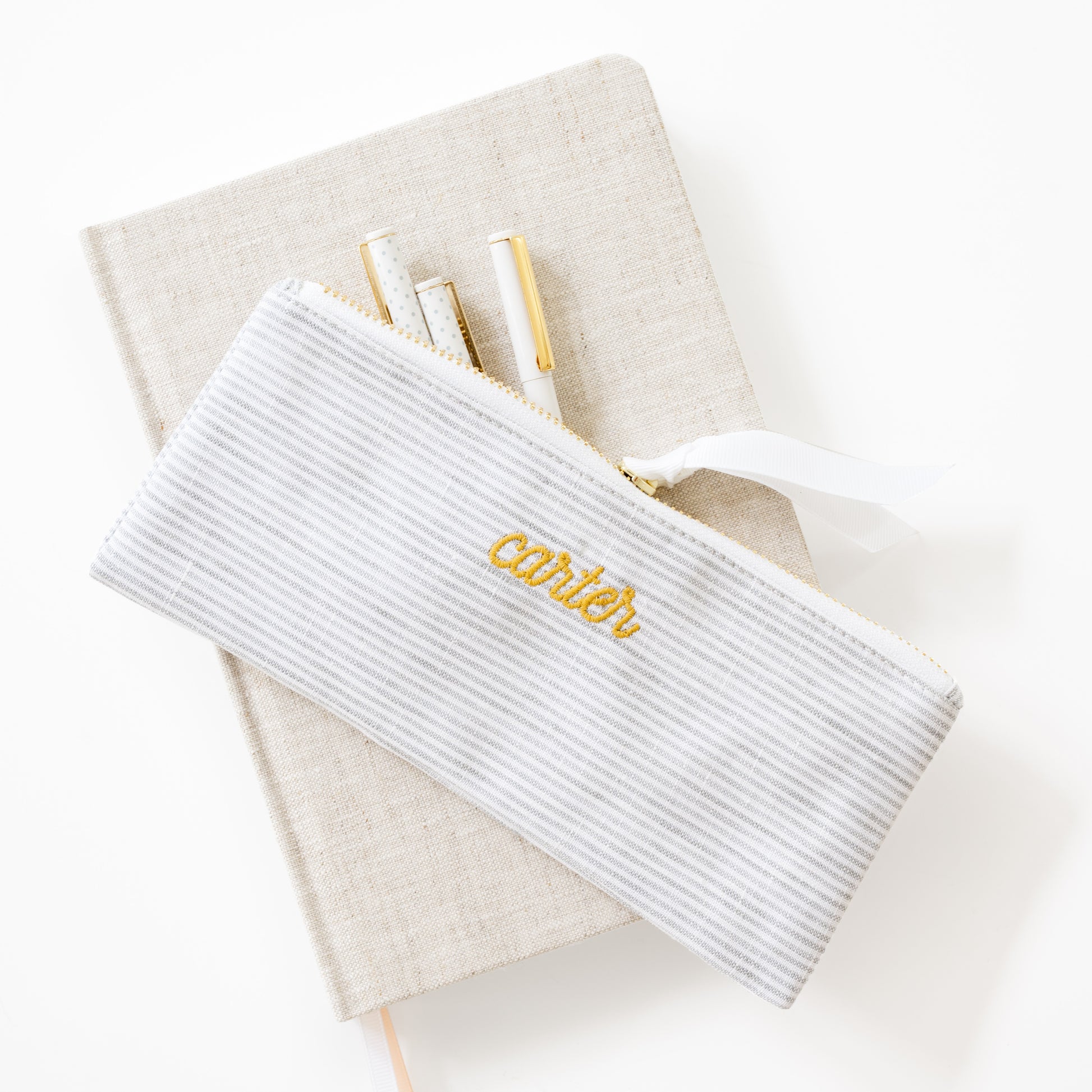 White stripe  pouch with 'carter' embroidery on a beige fabric journal with pens inside