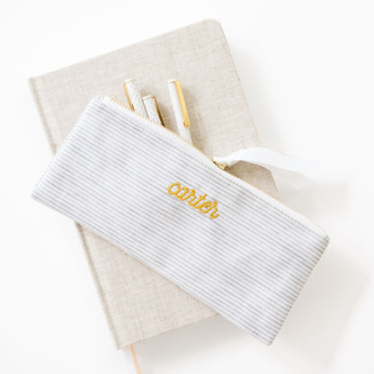 White stripe  pouch with 'carter' embroidery on a beige fabric journal with pens inside