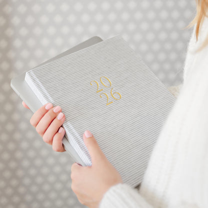 Grey stripe fabric planner with '26' in gold foil on the cover in hands