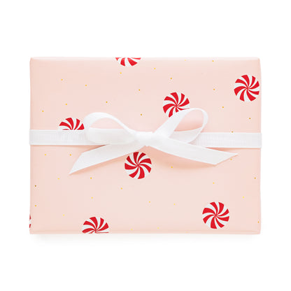 Pink gift wrap with tiny gold dots and peppermint candy with a white bow