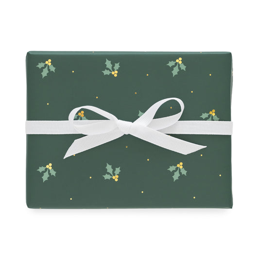 A rectangular gift box wrapped in dark green holiday paper with a white ribbon bow, featuring a pattern of small holly leaves, gold berries, and gold dots