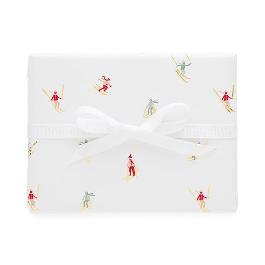 Wrapped gift with white with gold foil, red, pink and green skier pattern tied with a white ribbon bow