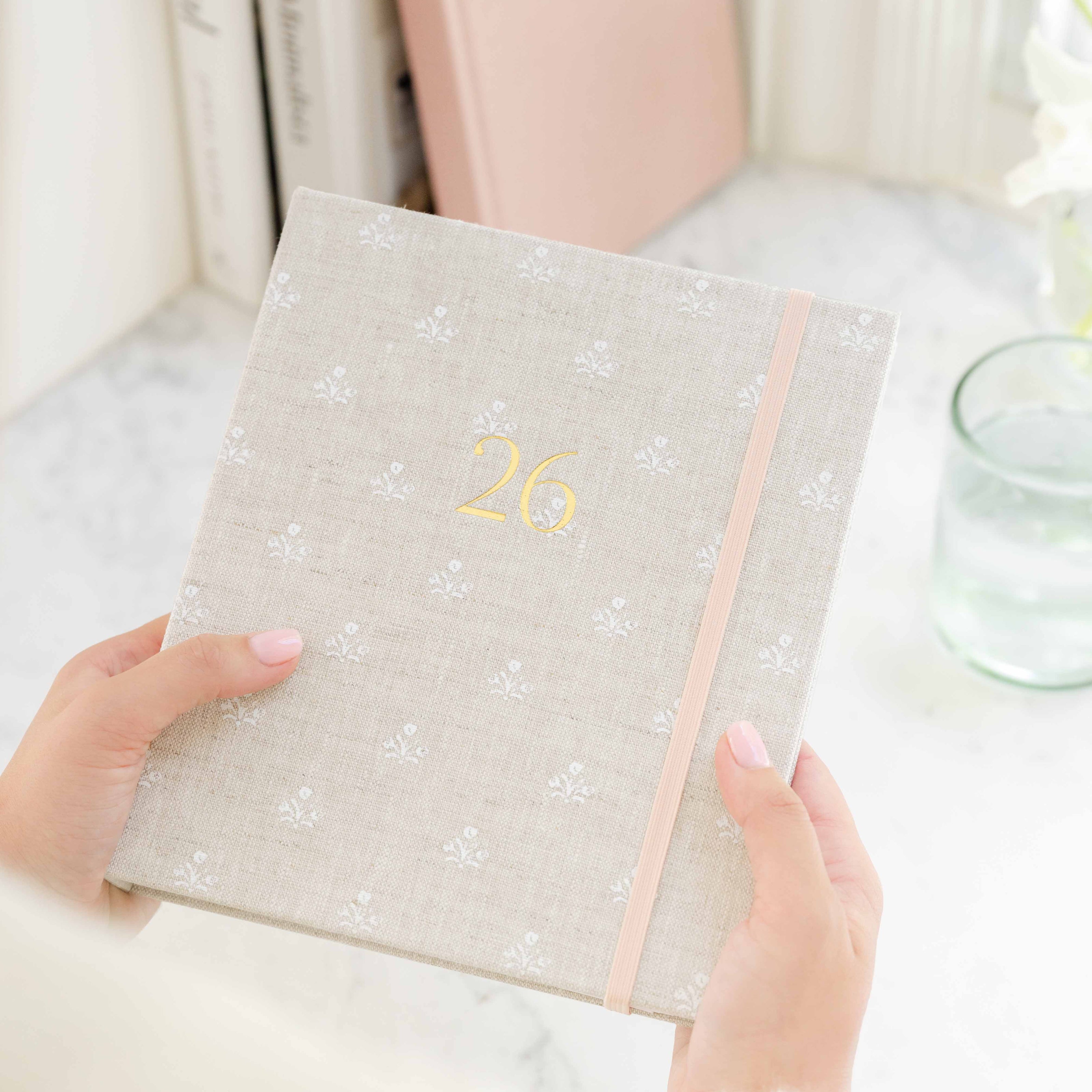 flax planner with gold "26" printed on the cover and pink elastic band