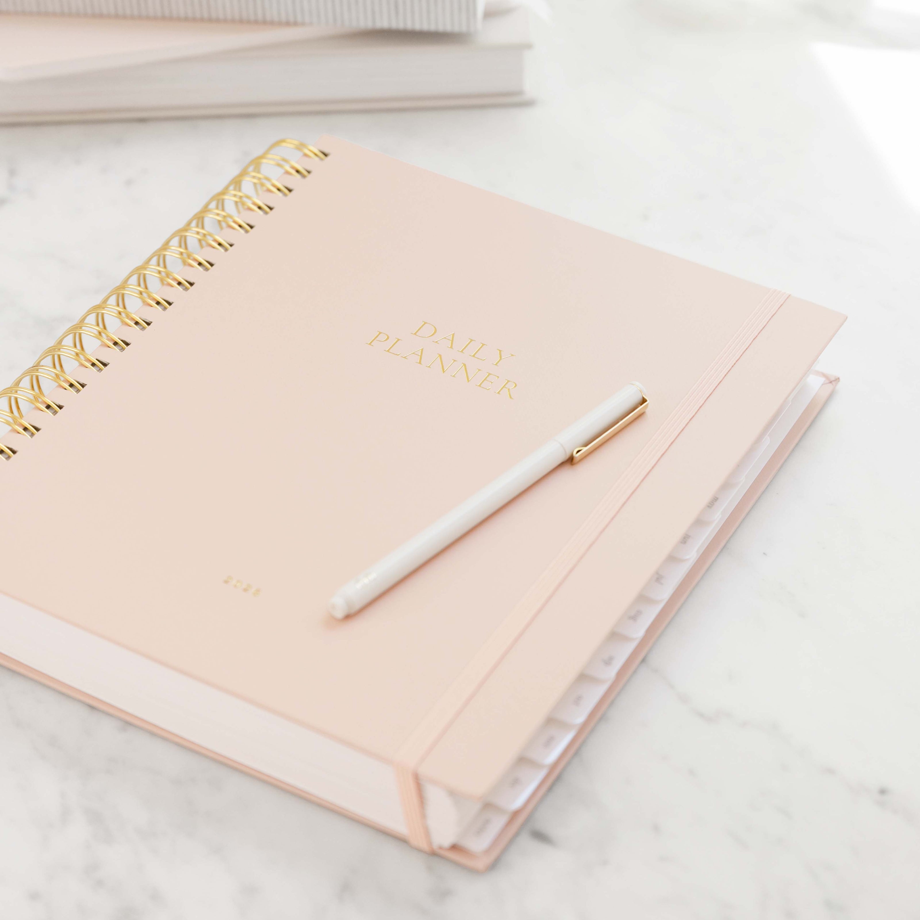 Pink planner with gold spiral binding and a white pen on a marble surface
