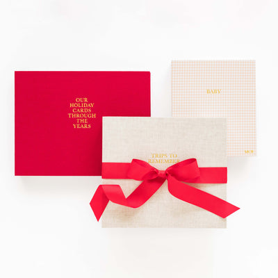 Red holiday card book, flax album, and pink check baby book with a red ribbon on a white background