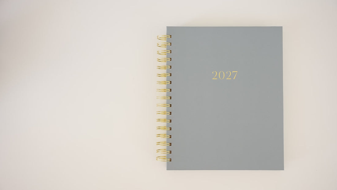 A person opening a 2027 blue signature spiral planner flipping through to show the interior page layouts