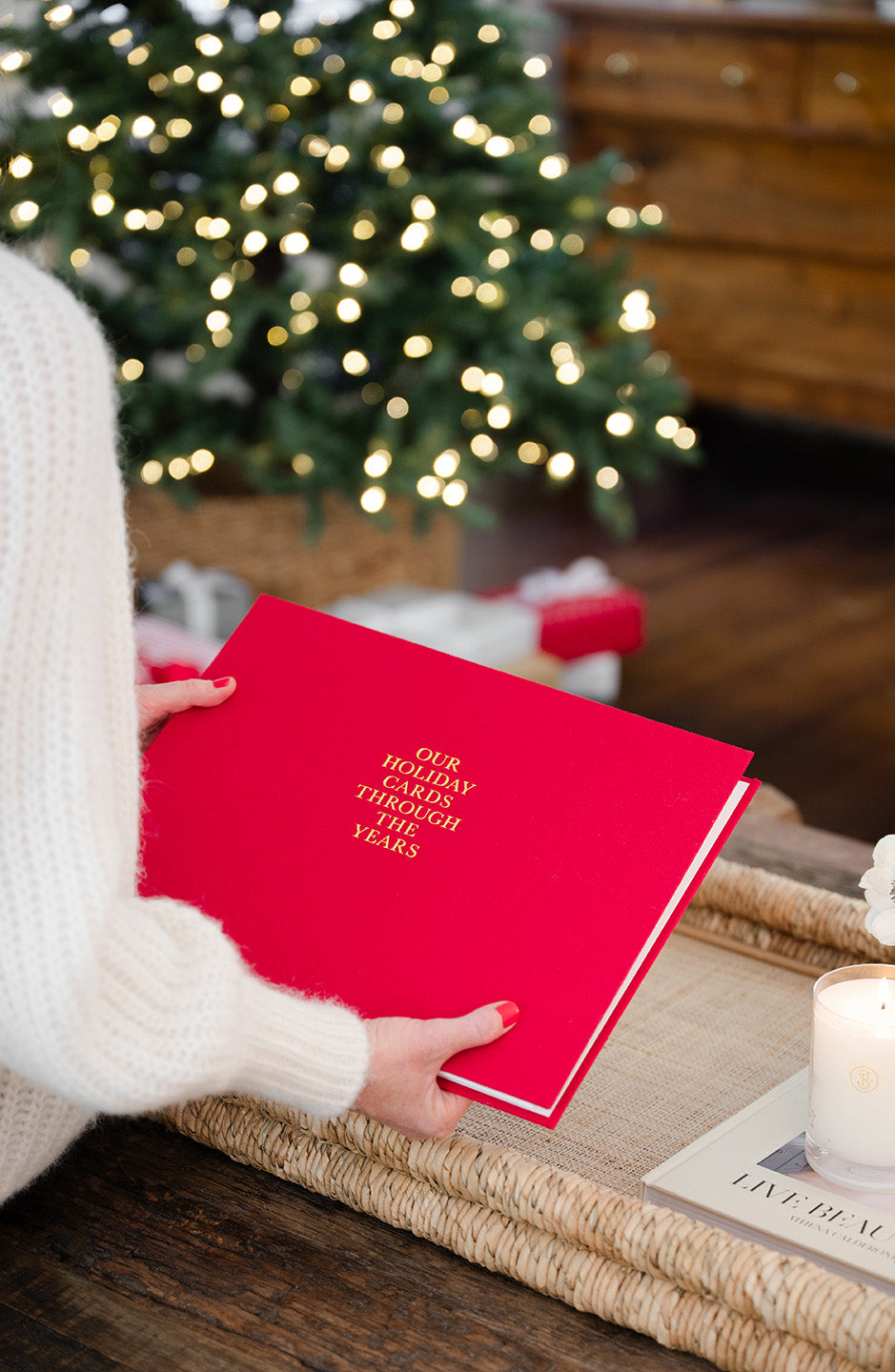 red holiday card book being placed on a coffee table with a christmas tree in the background