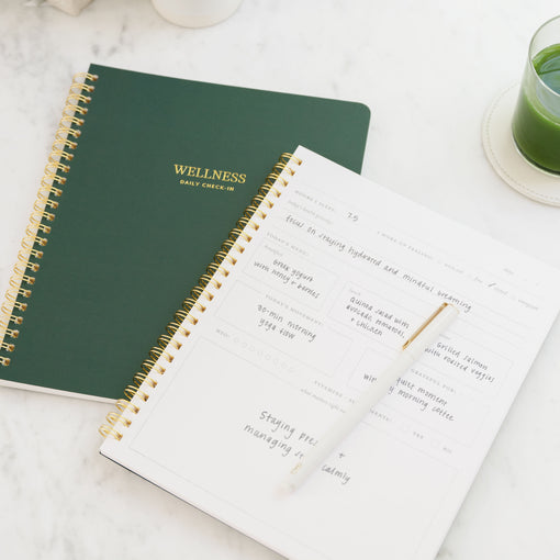 Wellness daily check-in notebook on a marble surface with a glass of green juice.