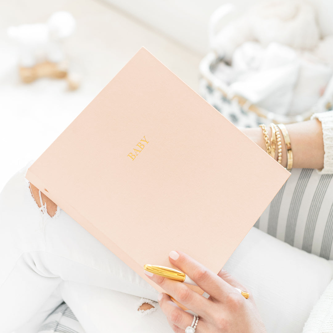 This shows the detail of the baby book with gold foil "baby" and pale pink fabric cover. 
