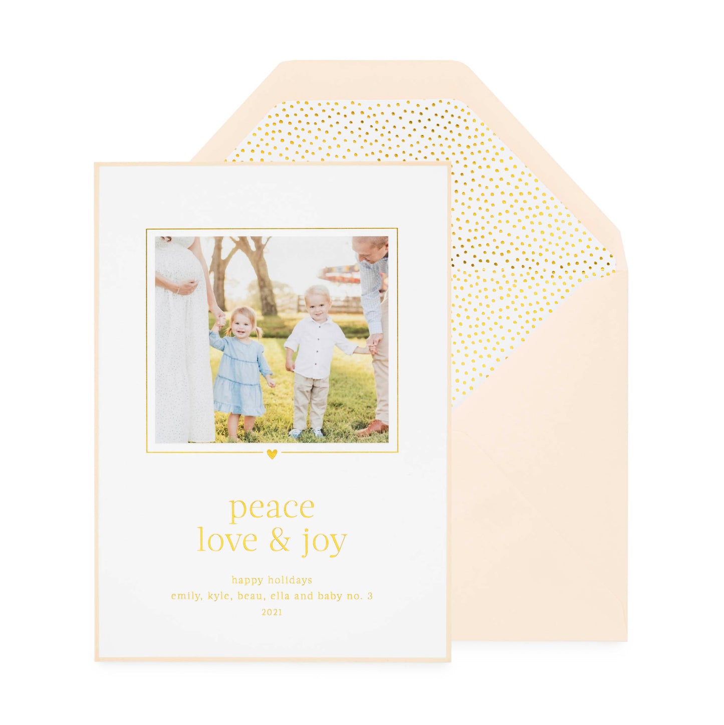 White custom holiday photo card printed with "peace love and joy" in gold foil with a photo of two kids and parents with a pink card border paired with a pink envelope open to gold teensy dot envelope liner