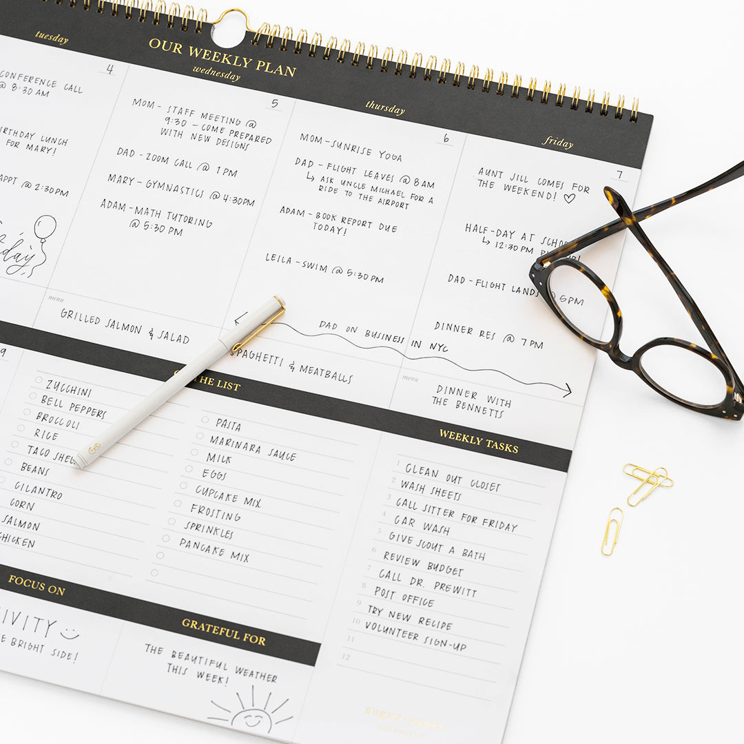 close up of our weekly plan pad with white felt pen, glasses, and gold paperclips