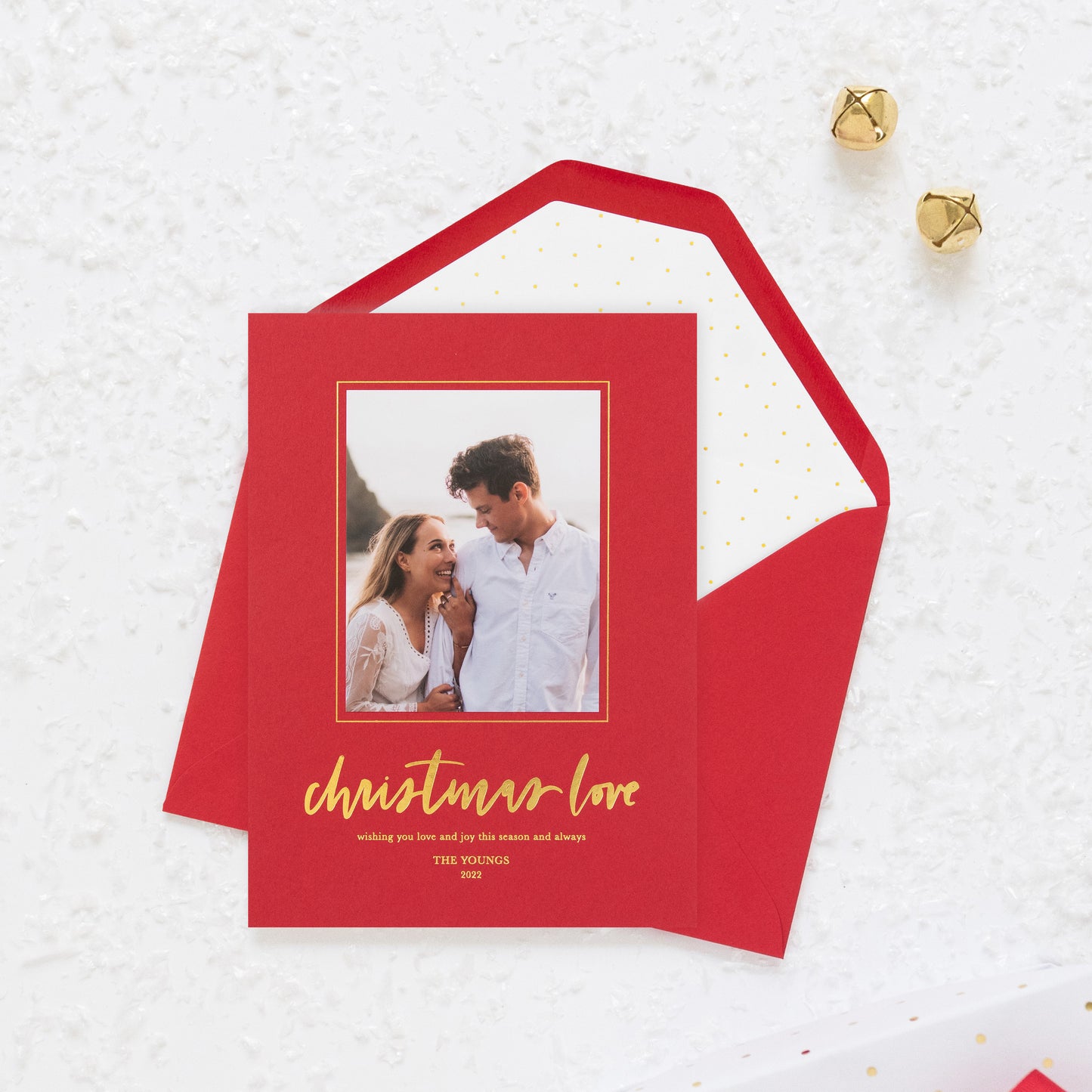 Red custom holiday photo card with photo of couple with greeting 'christmas love wishing you love and joy this season and always' paired with a white envelope with gold dots