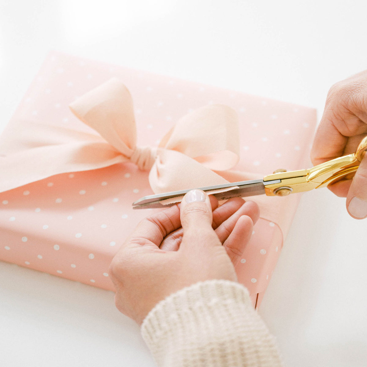 person trimming pale pink bow on rose dot wrapped gift