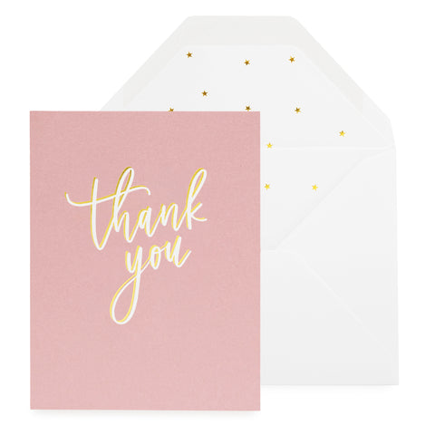 Dusty rose card printed with gold and white foil thank you in script paired with a white envelope with a gold star liner